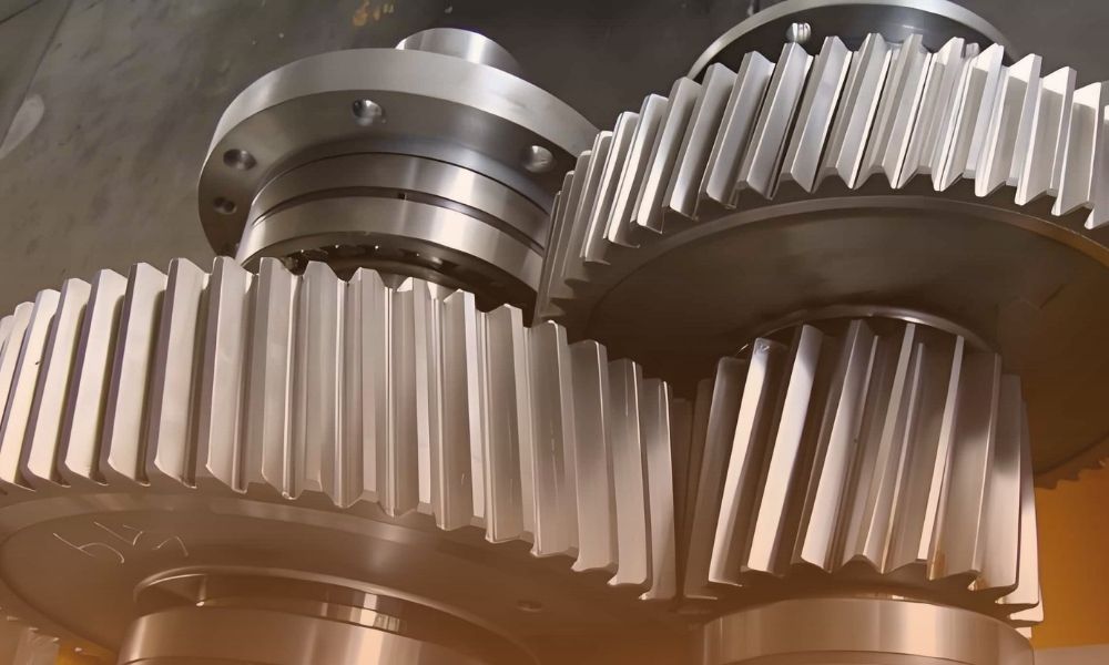 A close-up of large, metallic gears with evenly spaced teeth, stacked together in an industrial setting.