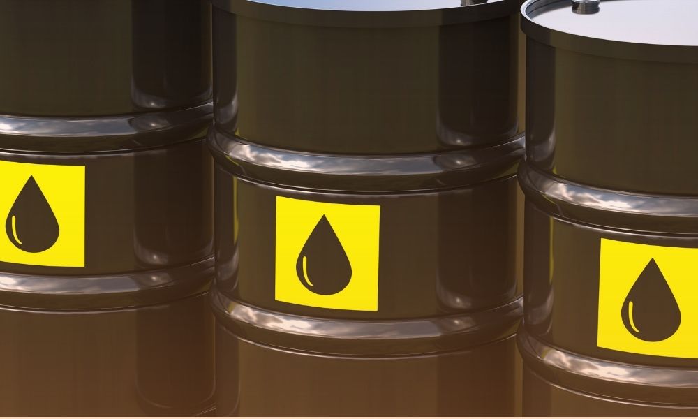 A close-up image of several black industrial barrels with yellow warning labels displaying a black droplet symbol, indicating they contain liquid hazardous materials. lubricant performance