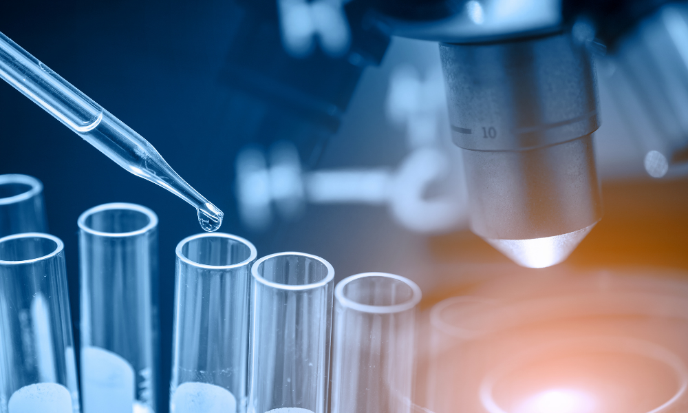 A close-up view of a laboratory scene with test tubes, a pipette dropping liquid into one of the test tubes, and a microscope in the background, illuminated by a soft light.