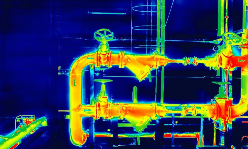 A thermal Infrared image of industrial piping and valves, showing temperature variations in the system with colors indicating heat levels, primarily in yellow, orange, and red against a dark blue background.
