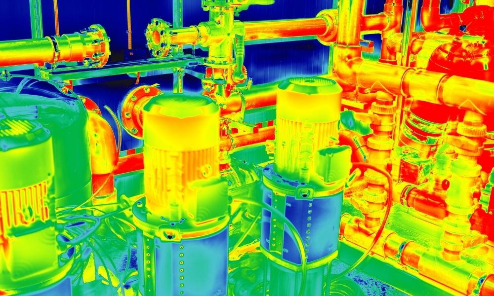 A thermal or infrared image of an industrial piping system with various pumps, valves, and pipes. The temperature is represented by a color gradient, with blue indicating cooler areas and red/yellow indicating hotter regions.