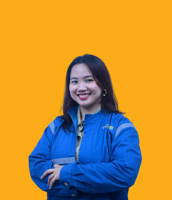A young woman with shoulder-length dark hair, smiling confidently with her arms crossed, wearing a blue jacket with reflective stripes and a beige shirt underneath, set against a solid orange background.