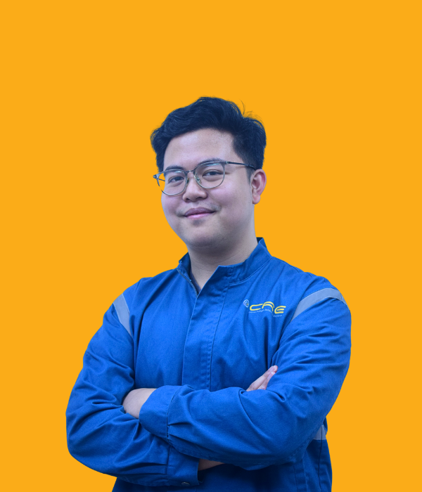 A young man with short black hair, wearing glasses and a blue jacket with a yellow logo, standing confidently with arms crossed against a bright orange background.