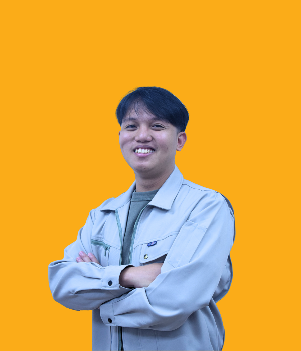 A young man with short black hair, smiling confidently with his arms crossed, wearing a light gray jacket over a green shirt, standing against an orange background.